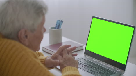 Mature-woman-nodding-her-head-yes-while-looking-at-a-green-screen-computer.-Elderly-mature-woman-with-gray-hair-and-a-video-call-on-her-Laptop.-Laptop-with-a-green-screen